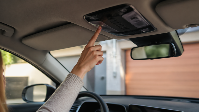 Driver using a Kia Sportage dashboard with HomeLink buttons and a garage door in the background