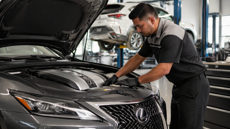 Technician working on a Lexus sedan in a dealership service bay with hood open